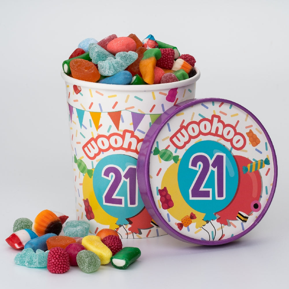 Candy Bucket 21 jaar gevuld met kleurrijke snoepjes, met het paarse deksel ernaast en losse snoepjes op de voorgrond.