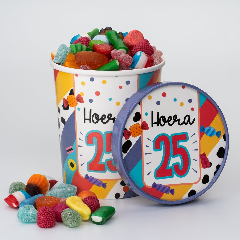 Candy Bucket 25 jaar gevuld met kleurrijke snoepjes, met het deksel ‘Hoera 25’ ernaast en losse snoepjes op de voorgrond.